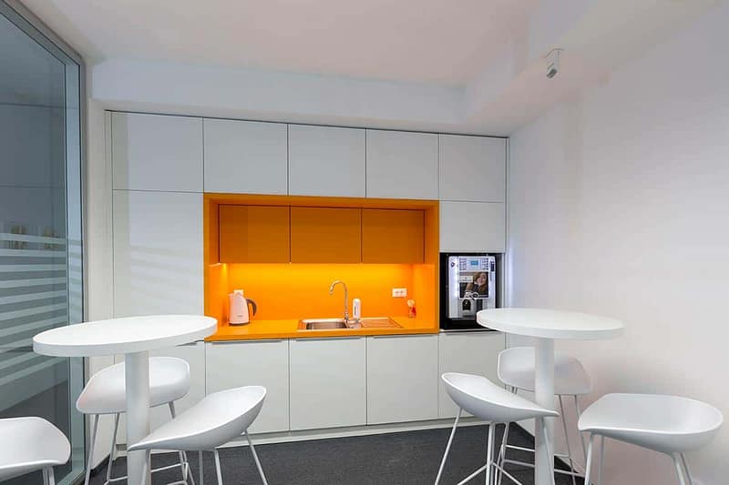 Modern office kitchenette with white cabinets and orange accents for business spaces.